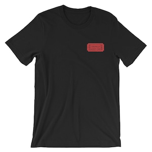 Op de afbeelding: Zwart T-shirt met een rood ticketontwerp met de tekst "Valhalla" en "Admit One".