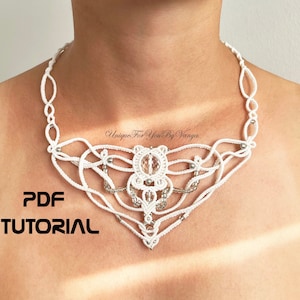 Può includere: Collana in crochet bianco con un accento di perline argentate e un centro in cristallo. La collana ha la forma di una farfalla. Il testo "PDF TUTORIAL" è stampato sull'immagine.