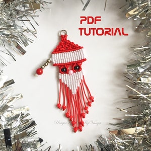以下が含まれることがあります： 赤い白のサンタクロースのオーナメントは、ひもといくつかのビーズで作られています。オーナメントは白いひげとピンクの鼻をしています。オーナメントは銀色のガーランドにぶら下がっています。テキスト「PDF TUTORIAL」は白い背景に黒い文字で書かれています。