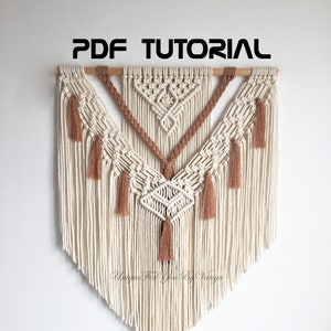 May include: A beige and brown macrame wall hanging with tassels. The wall hanging is in the shape of a triangle and has a wooden dowel at the top. The text "PDF TUTORIAL" is written in black at the top of the image.