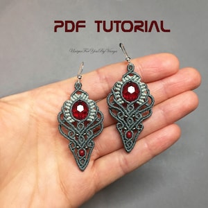 Op de afbeelding: Een paar grijze en rode kralen oorbellen met een rood kristal in het midden. De oorbellen hangen aan zilveren haken. De oorbellen zijn op een hand, en de tekst "PDF TUTORIAL Unique For You By Vanya" staat boven de oorbellen.