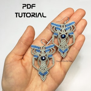 May include: A pair of gray and blue macrame earrings with a dark blue gemstone accent. The earrings are hanging from silver ear wires. The earrings are being held in a hand. The image includes the text "PDF TUTORIAL" and "Unique For You By Vanja".
