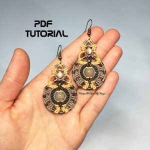 Peut inclure: Une paire de boucles d'oreilles faites à la main avec un motif en macramé. Les boucles d'oreilles sont faites avec un cordon brun et beige et présentent une pierre ronde de couleur brun clair au centre. Les boucles d'oreilles sont suspendues à un crochet en bronze.
