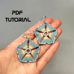 May include: A pair of handmade macrame flower earrings in pastel colors of blue, teal, and peach. The earrings are in the shape of a five-petal flower with a silver hook. The image also includes the text "PDF TUTORIAL".