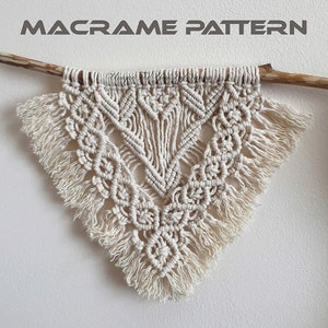 May include: A white macrame wall hanging with a triangular shape and fringe details. The hanging is made with a knotting technique and is attached to a wooden dowel.