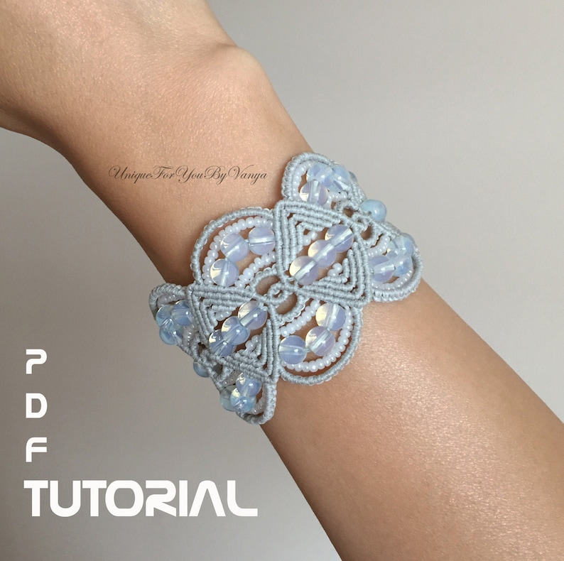 Puede incluir: Un brazalete de macram&eacute; gris con cuentas blancas. El brazalete est&aacute; atado en un patr&oacute;n de nudos y tiene un dise&ntilde;o floral. El texto "Unique For You By Vanya" es visible en la imagen.  PDF TUTORIAL