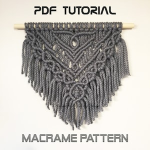 May include: Gray macrame wall hanging with a geometric pattern and fringe. The hanging is attached to a wooden dowel. "PDF TUTORIAL" and "MACRAME PATTERN" are written in black text at the top and bottom of the image.