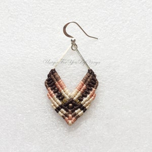 K&ouml;nnte beinhalten: Ein einzelner Makramee-Ohrring mit geometrischem Design. Der Ohrring hat ein rautenf&ouml;rmiges Webmuster in Braun-, Beige- und Rosat&ouml;nen mit einem silberfarbenen Metallhaken. Der Text "Unique For You By Vanya" ist sichtbar.