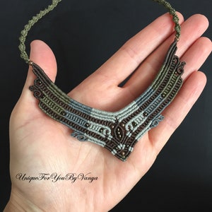May include: A brown, grey and green macrame necklace with small brown beads. The necklace is in the shape of a V and has a delicate, intricate design.