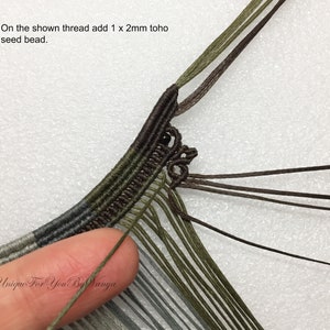 May include: Close-up of a macrame project with multiple strands of green, brown, and grey thread. A single 2mm toho seed bead is being added to the thread.