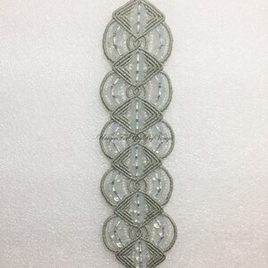 Puede incluir: Un brazalete de macram&eacute; gris con cuentas blancas y cierres plateados. "Unique For You By Vinya" est&aacute; escrito en el brazalete.