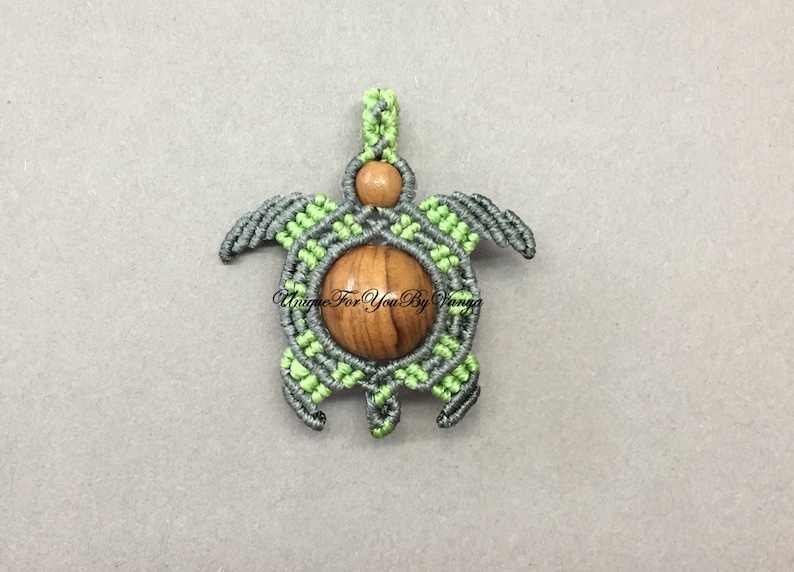 May include: A green and gray macrame turtle pendant with a wooden bead in the center. The pendant is made with a knotting technique.