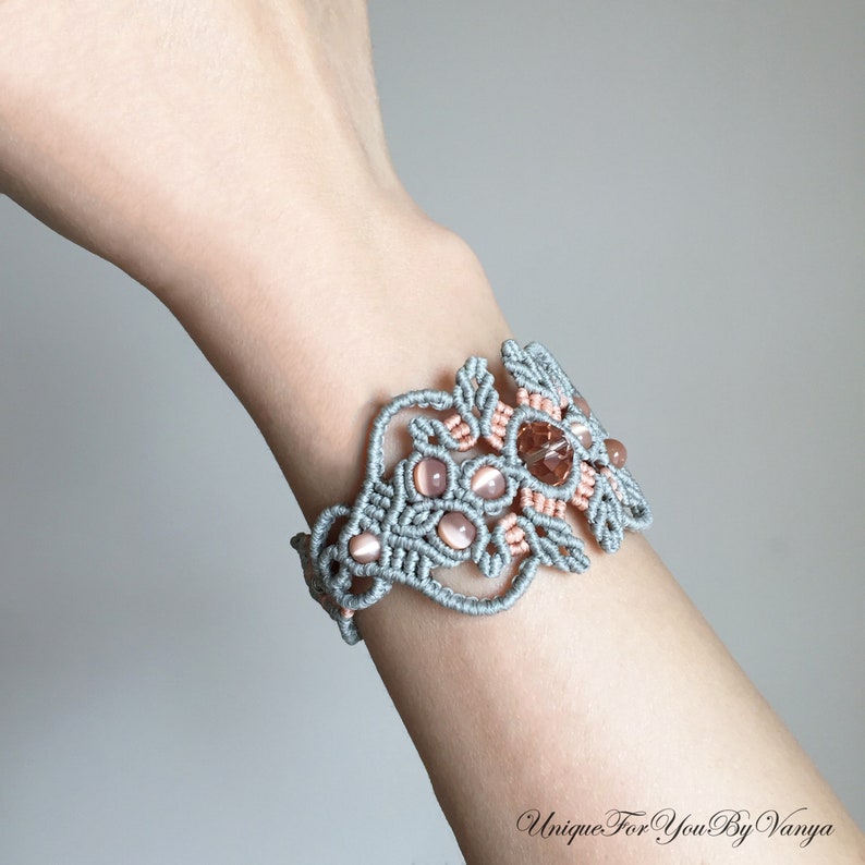 May include: A gray and peach macrame bracelet with pink and clear gemstone beads. The bracelet is tied in a knot pattern and features a floral design.