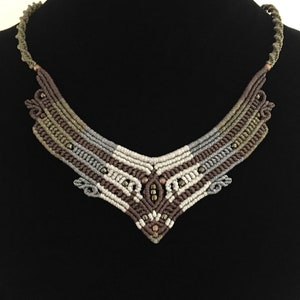 May include: A brown, grey and white macrame necklace with copper beads. The necklace is in the shape of a V and has a geometric pattern.