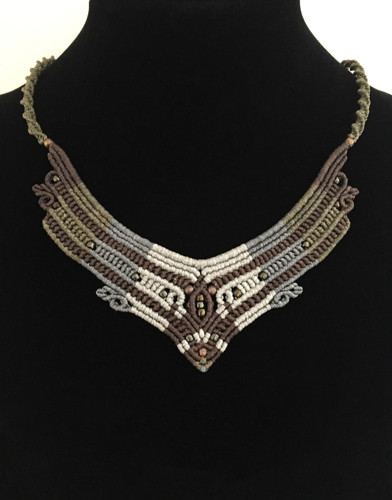 May include: A brown, grey and white macrame necklace with copper beads. The necklace is in the shape of a V and has a geometric pattern.