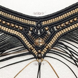 May include: Close-up of a black and brown macrame necklace with gold beads and a clear crystal pendant. The necklace is made with a knotting technique and has a fringe at the bottom.
