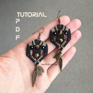 May include: A pair of black and brown macrame earrings with tiger's eye and black beads, and gold leaf accents. The earrings are hanging from a hand. The image includes the text "TUTORIAL PDF".
