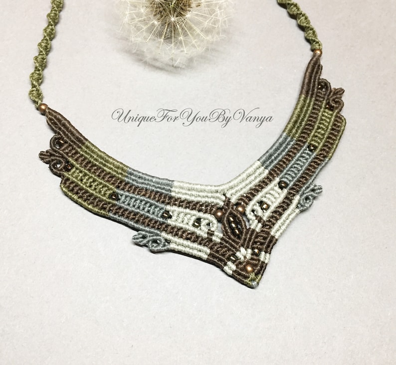 May include: A brown, green and grey macrame necklace with a geometric design and copper beads. The necklace is made with a variety of cords and beads, creating a unique and intricate pattern.