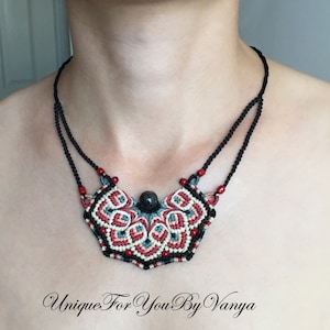 Może przedstawiać: Czarny sznurek z naszyjnikiem z czerwono-biało-niebieskim makramowym wisiorem z ciemnoniebieskim kamieniem szlachetnym w środku. Wisiorek ma kształt p&oacute;łksiężyca. Tekst "Unique For You By Vanya" jest widoczny na dole obrazu.