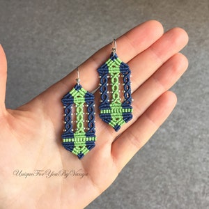May include: A pair of green and blue macrame earrings with silver beads. The earrings are hanging from silver hooks.