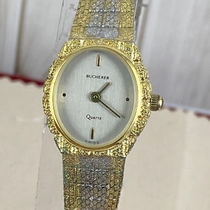 Op de afbeelding: Een gouden Bucherer quartz polshorloge met een witte wijzerplaat en een getextureerde gouden band.