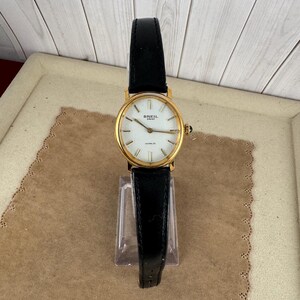K&ouml;nnte beinhalten: Eine goldfarbene Armbanduhr von Breil Milano mit wei&szlig;em Zifferblatt und schwarzem Lederarmband.