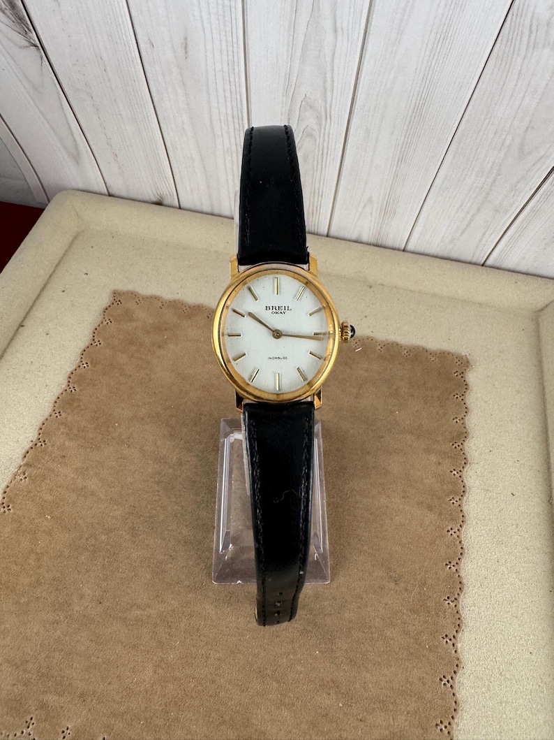 K&ouml;nnte beinhalten: Eine goldfarbene Armbanduhr von Breil Milano mit wei&szlig;em Zifferblatt und schwarzem Lederarmband.