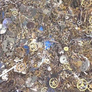 May include: A close-up view of a blue bin filled with a variety of small, intricate watch parts. The parts are primarily metallic, with shades of gold, silver, and bronze. The collection includes gears, plates, and other components, suggesting a supply for repair or crafting.