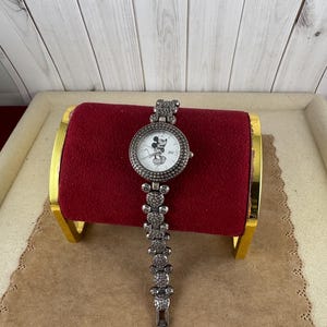 Puede incluir: Un reloj plateado con una esfera blanca y un dise&ntilde;o de Mickey Mouse. El reloj tiene una correa plateada con un dise&ntilde;o de Mickey Mouse.