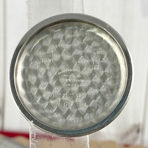 May include: The back of a silver wristwatch with a patterned dial. The watch has the text "MONOCHRON" "SWITZERLAND" "PRECISION" "2000" and the numbers "A22677" and "16491".