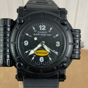 May include: Black Casio Pathfinder wristwatch with a yellow and black face. The watch has a black rubber band and a black metal case. The watch face has the words "CASIO" and "PATHFINDER" on it. The watch is water resistant to 50 meters.