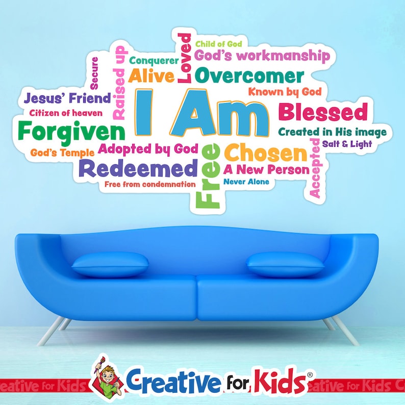 Op de afbeelding: Een blauwe bank met twee kussens staat onder een muursticker. De sticker toont de woorden "I Am" in grote blauwe letters, omringd door woorden als "Forgiven", "Blessed" en "Chosen". De sticker is veelkleurig.