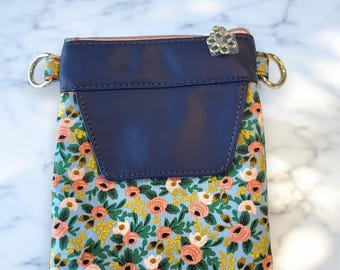 May include: A small blue and floral patterned crossbody bag with a navy blue flap and a silver zipper pull.