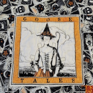 May include: A black and white quilt with a large orange square in the centre. The square has a black and white illustration of a witch with the text "GOOSE TALES" above and below the image.
