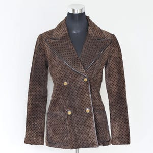 May include: A brown double-breasted blazer with a repeating geometric pattern. The blazer has a notched collar, two front pockets, and gold-colored buttons. The edges are trimmed with a darker brown material.