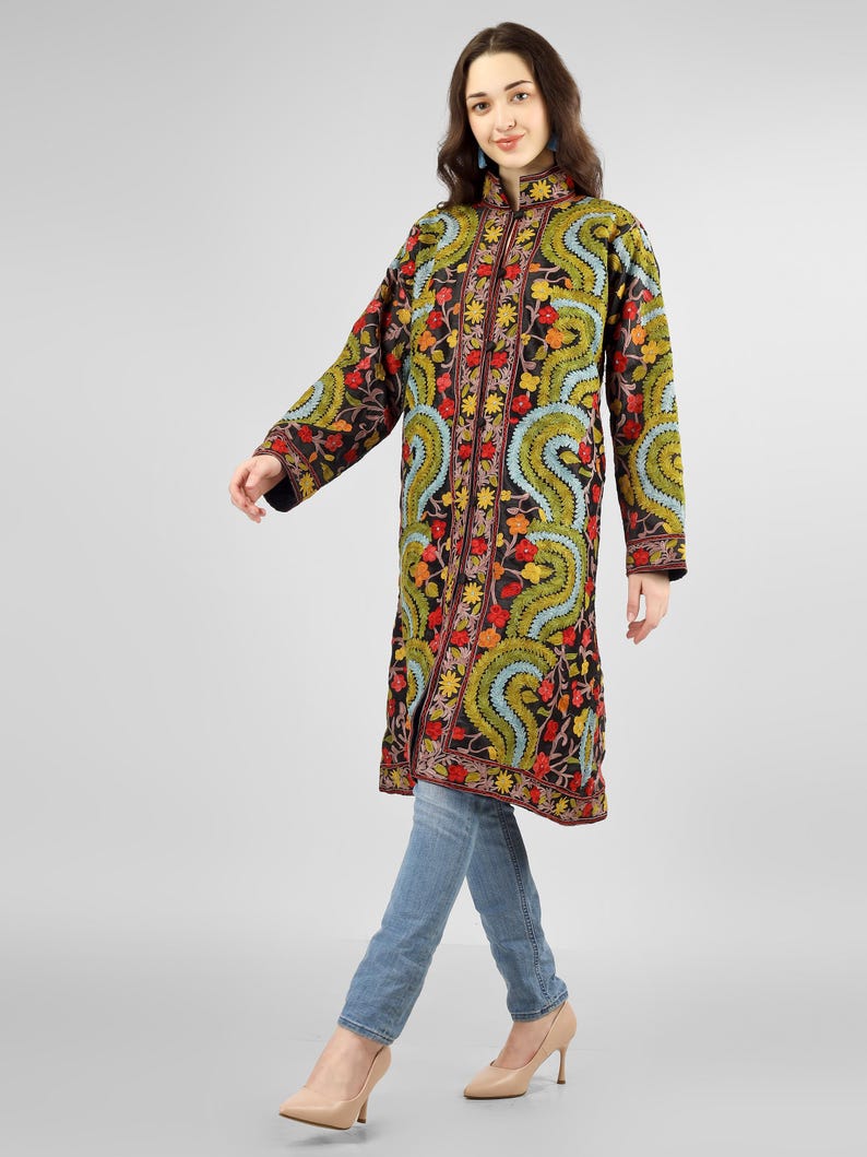 May include: A long black embroidered coat with a mandarin collar and floral patterns in shades of red, yellow, green, and blue. The coat is worn over blue jeans.