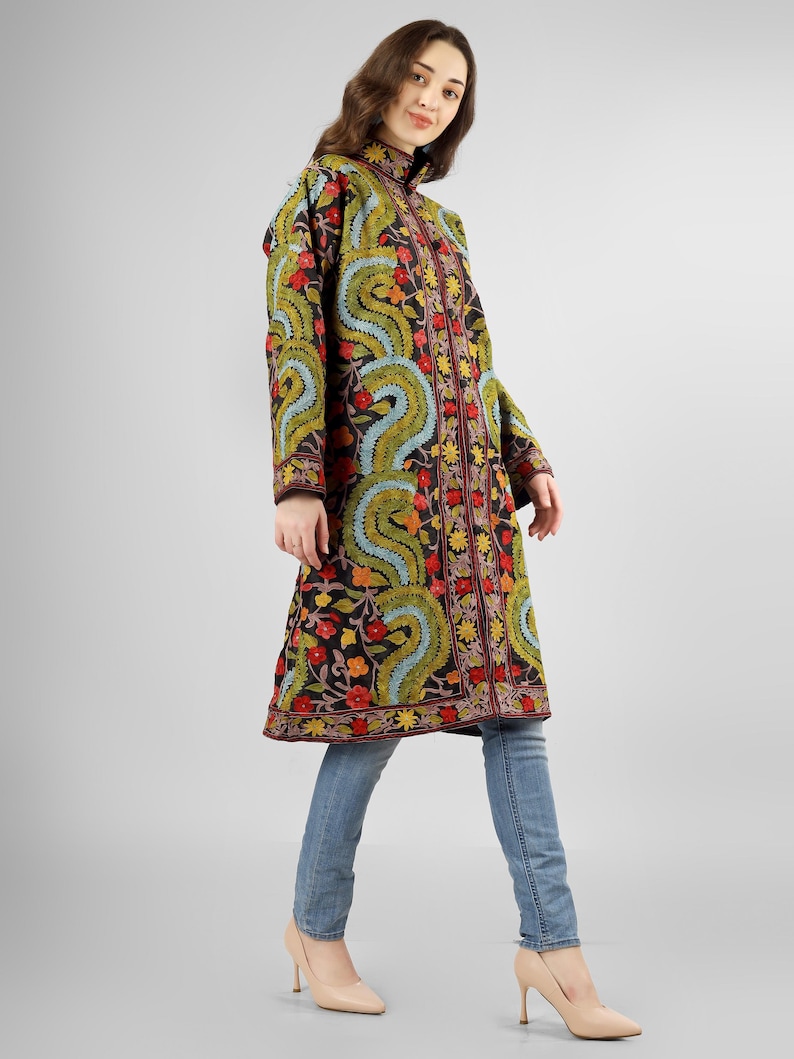May include: A long black embroidered coat with a floral and paisley design in shades of red, green, blue, and yellow. The coat has a high collar and a button closure.