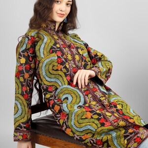May include: A long black embroidered jacket with a floral pattern in shades of red, green, blue, and yellow. The jacket has a mandarin collar and a button closure.