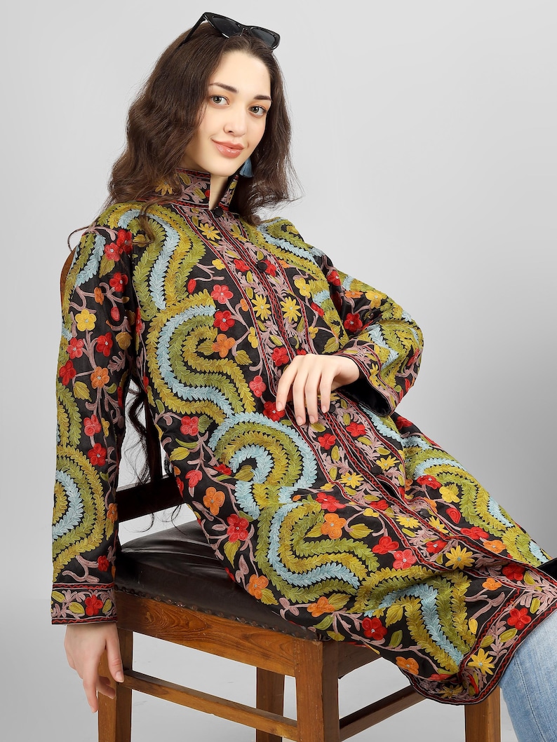 May include: A long black embroidered jacket with a floral pattern in shades of red, green, blue, and yellow. The jacket has a mandarin collar and a button closure.