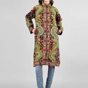May include: A long black coat with colorful floral embroidery. The coat has a mandarin collar and a button closure. The model is wearing blue jeans and heels.
