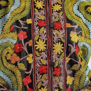 May include: A black silk jacket with intricate floral embroidery in shades of red, yellow, green, and blue. The jacket features a mandarin collar and a button closure.