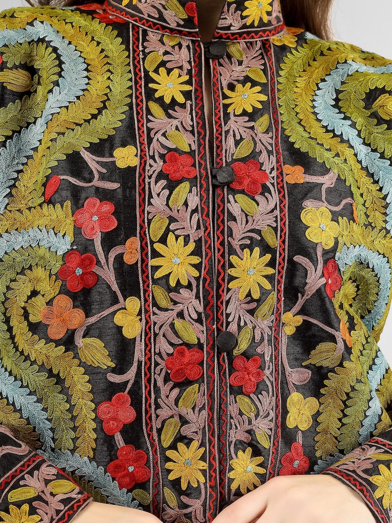 May include: A black silk jacket with intricate floral embroidery in shades of red, yellow, green, and blue. The jacket features a mandarin collar and a button closure.