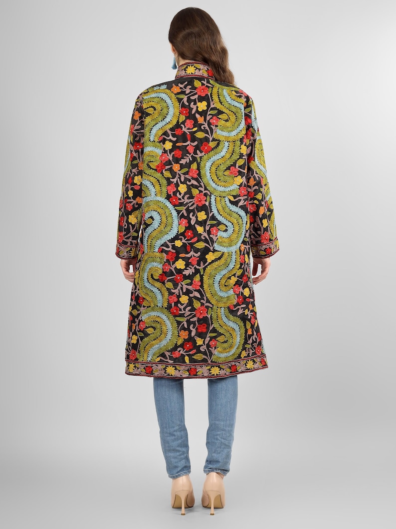 May include: A long black embroidered coat with a floral and paisley pattern in shades of red, green, blue, and yellow. The coat has a mandarin collar and long sleeves.
