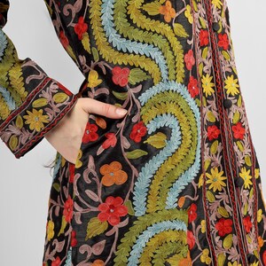 May include: A black long-sleeved jacket with intricate floral embroidery in shades of red, yellow, green, and blue. The jacket has a button-up front and a pocket on the left side.