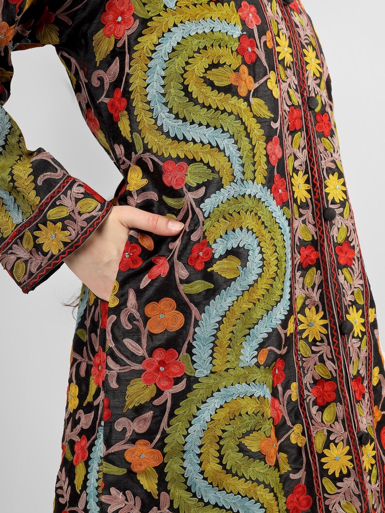 May include: A black long-sleeved jacket with intricate floral embroidery in shades of red, yellow, green, and blue. The jacket has a button-up front and a pocket on the left side.