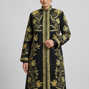 Op de afbeelding: Een zwarte jas met lange mouwen, een opstaande kraag en een knoopsluiting aan de voorzijde. De jas is versierd met gedetailleerd goudkleurig borduurwerk in een bloemen- en bladpatroon dat over de voorpanden, de mouwen en de kraag loopt.