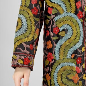 May include: A long black jacket with colorful floral embroidery. The embroidery features a variety of colors, including red, orange, yellow, green, blue, and pink. The jacket has a long sleeve and a button-up front.