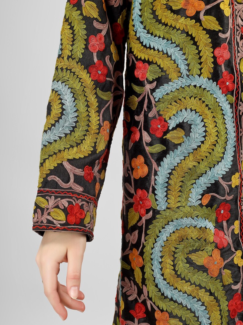 May include: A long black jacket with colorful floral embroidery. The embroidery features a variety of colors, including red, orange, yellow, green, blue, and pink. The jacket has a long sleeve and a button-up front.