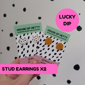 May include: Two pairs of handmade polymer clay stud earrings. One pair is white with black polka dots and the other pair is a mustard yellow hexagon shape. The earrings are displayed on white cards with black polka dots and the text "HOUSE OF HETTY handmade polymer clay accessories". The cards are held in a hand with the text "STUD EARRINGS X2" in pink.