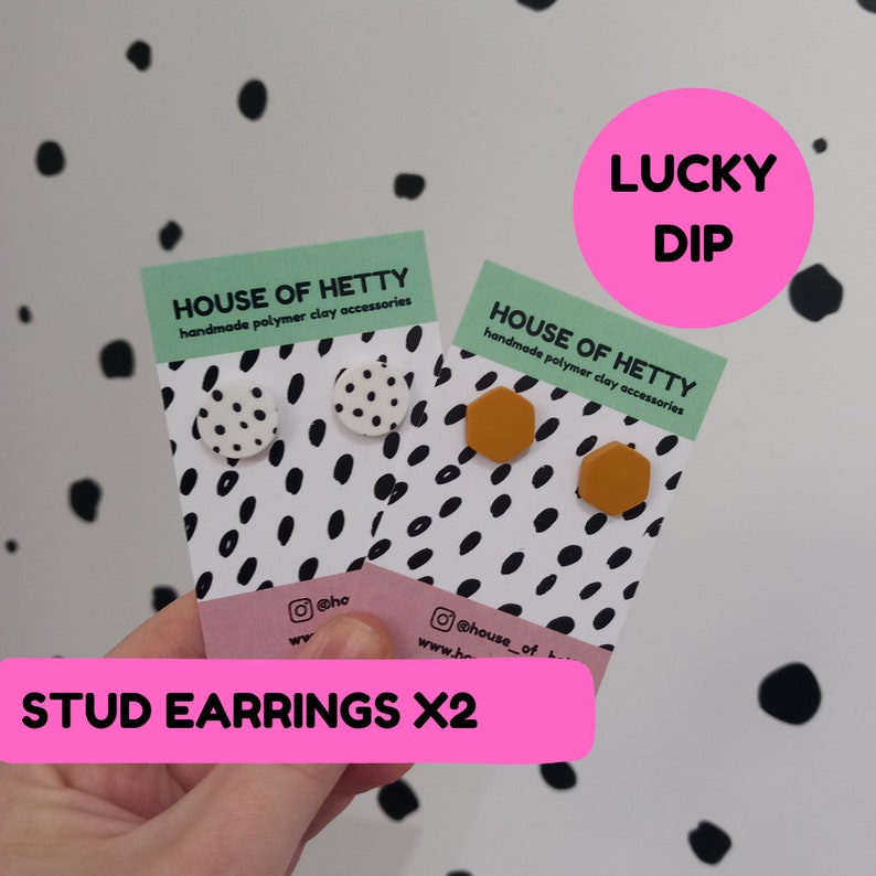 May include: Two pairs of handmade polymer clay stud earrings. One pair is white with black polka dots and the other pair is a mustard yellow hexagon shape. The earrings are displayed on white cards with black polka dots and the text "HOUSE OF HETTY handmade polymer clay accessories". The cards are held in a hand with the text "STUD EARRINGS X2" in pink.